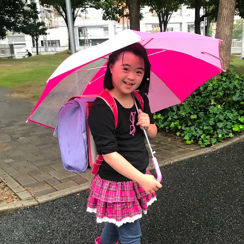傘を差し、笑顔でこちらを振り返っているダウン症の女の子